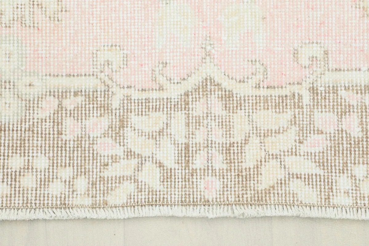 Close-up of the rug's border showing beige and rose floral motifs and fringe
