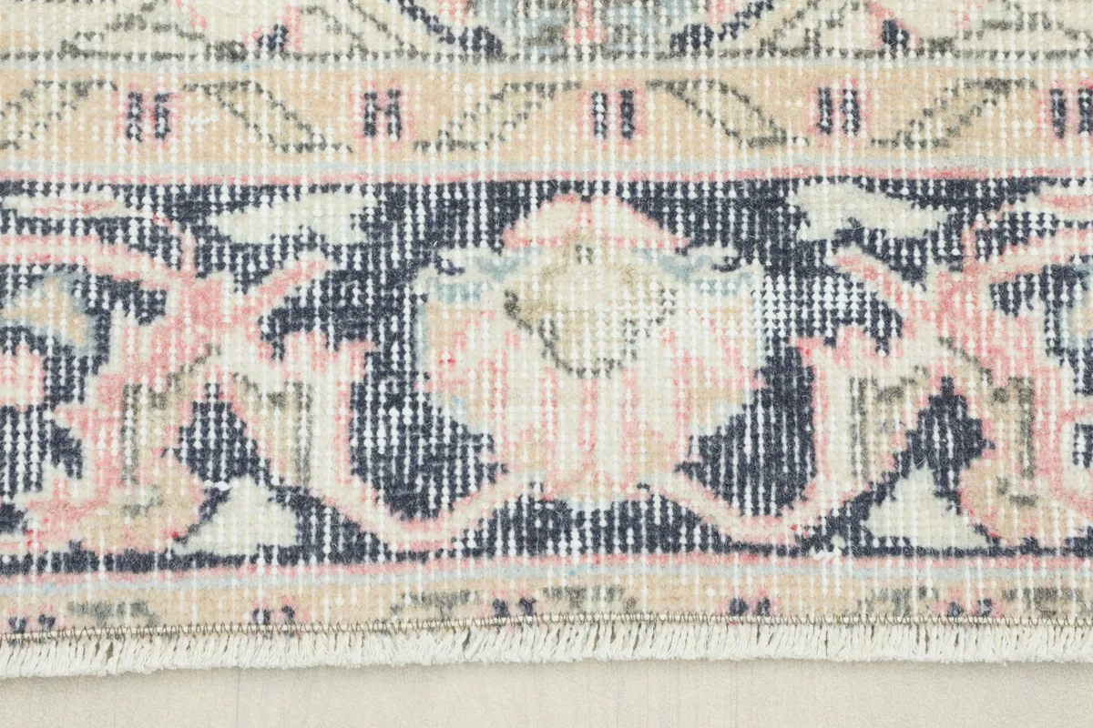 Close-up detail of the rug's border showing navy, rose, and beige tones