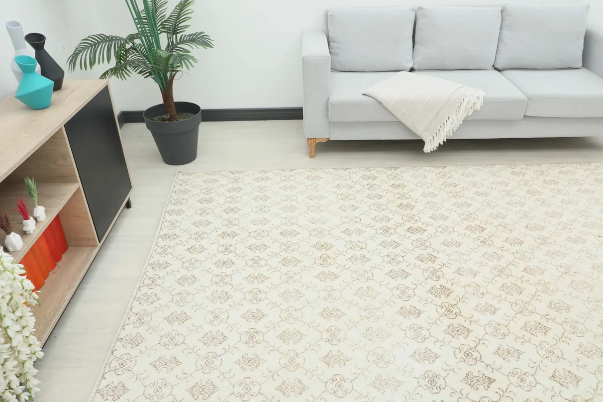 Angle shot of the cream and tan rug in a living space, showing its size relative to a sofa and cabinet.