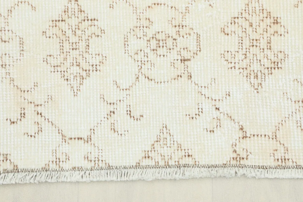Close-up view of the rug's short fringe and the repeating tan geometric pattern on a cream field.