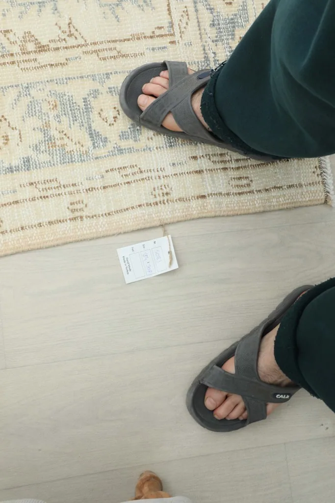 Feet in sandals next to the rug, showing scale and texture close to the floor