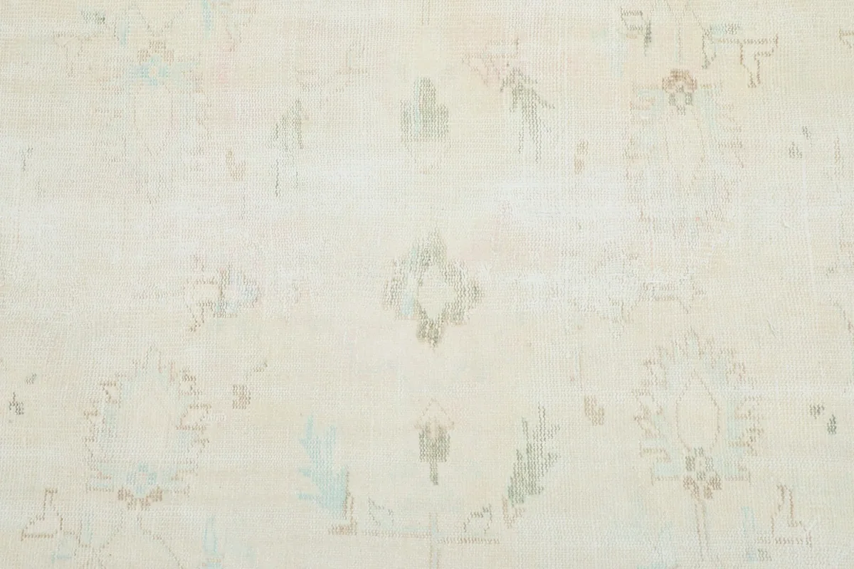 Detailed view of the subtle, faded floral and geometric patterns on the ivory rug's surface