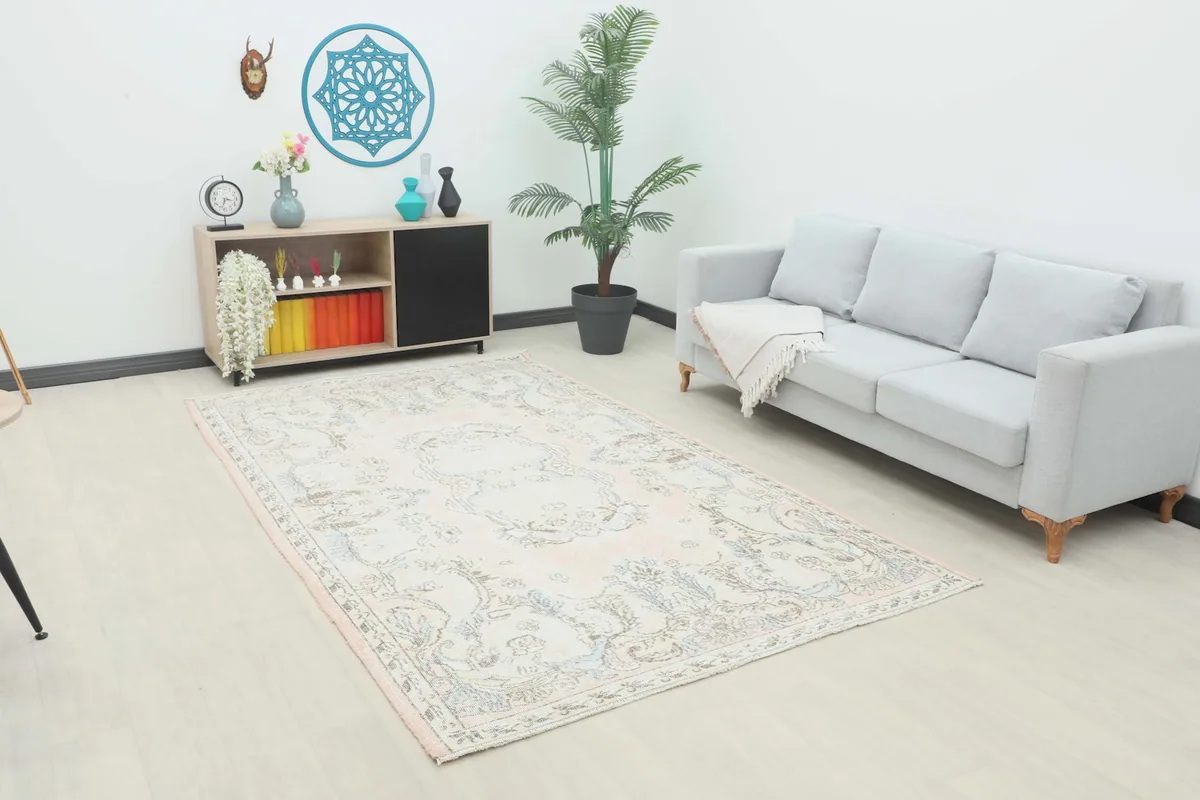 Vintage rose and blue Anatolian rug displayed in a bright living room setup with a gray sofa