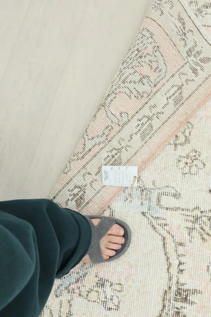 Overhead view of a foot next to the rug's reverse side, showing its label and foundation