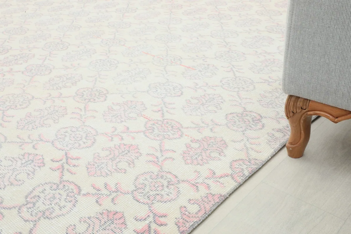 Partial view of the rug extending into a room, next to the leg of a piece of furniture.