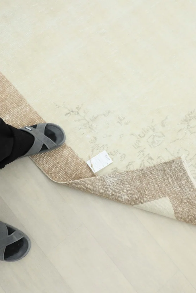 A foot in a sandal next to the rug's edge, showing the low pile and tag.