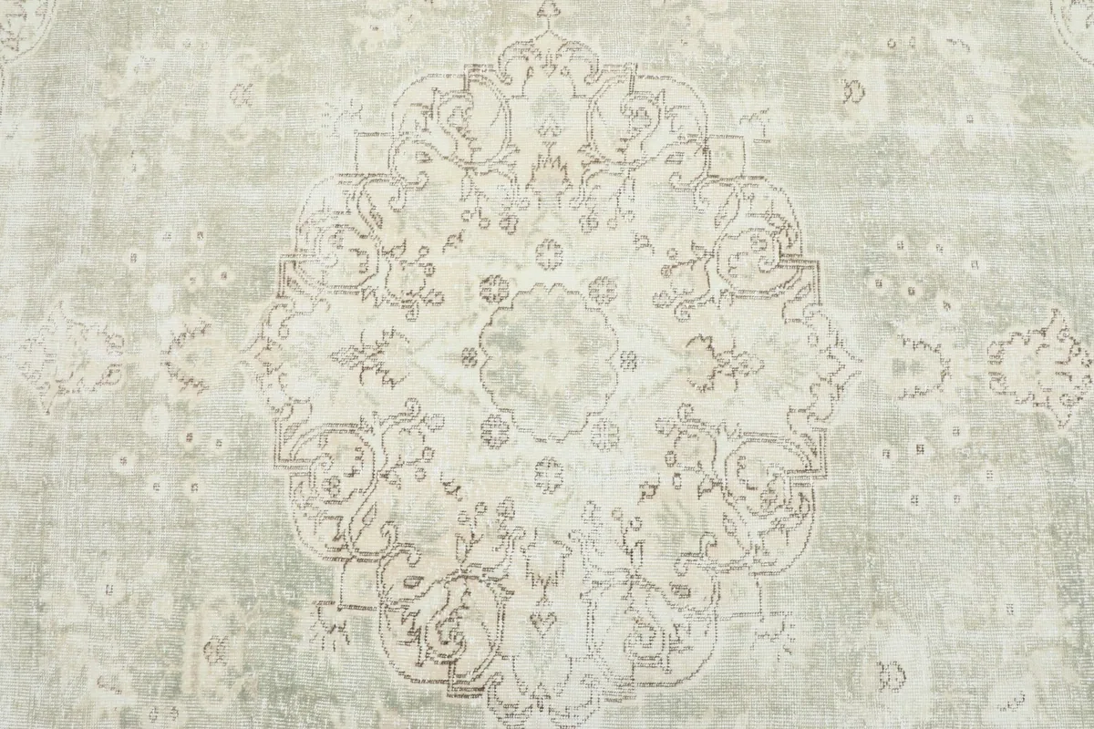 Detailed view of the central medallion design with faded green and beige wool pile.