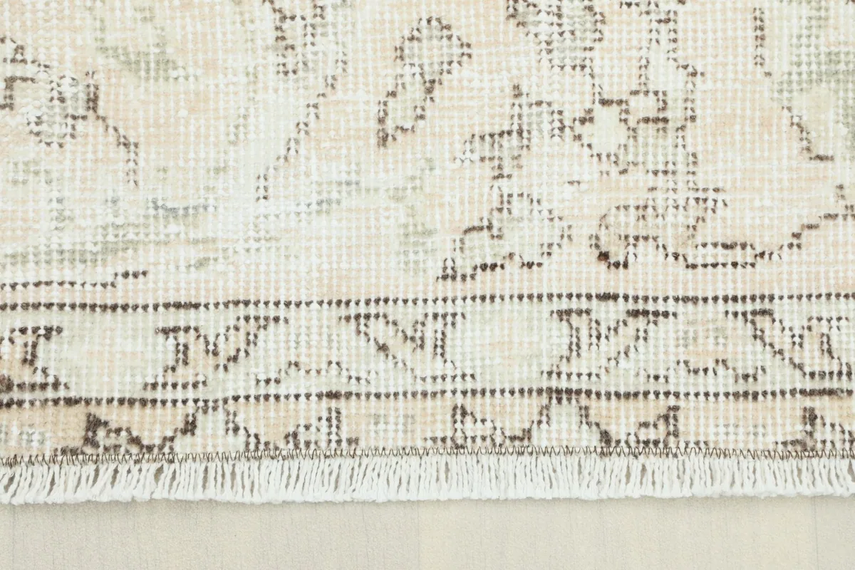 Close-up view of the rug's border showing the faded beige and brown tones and short fringe.