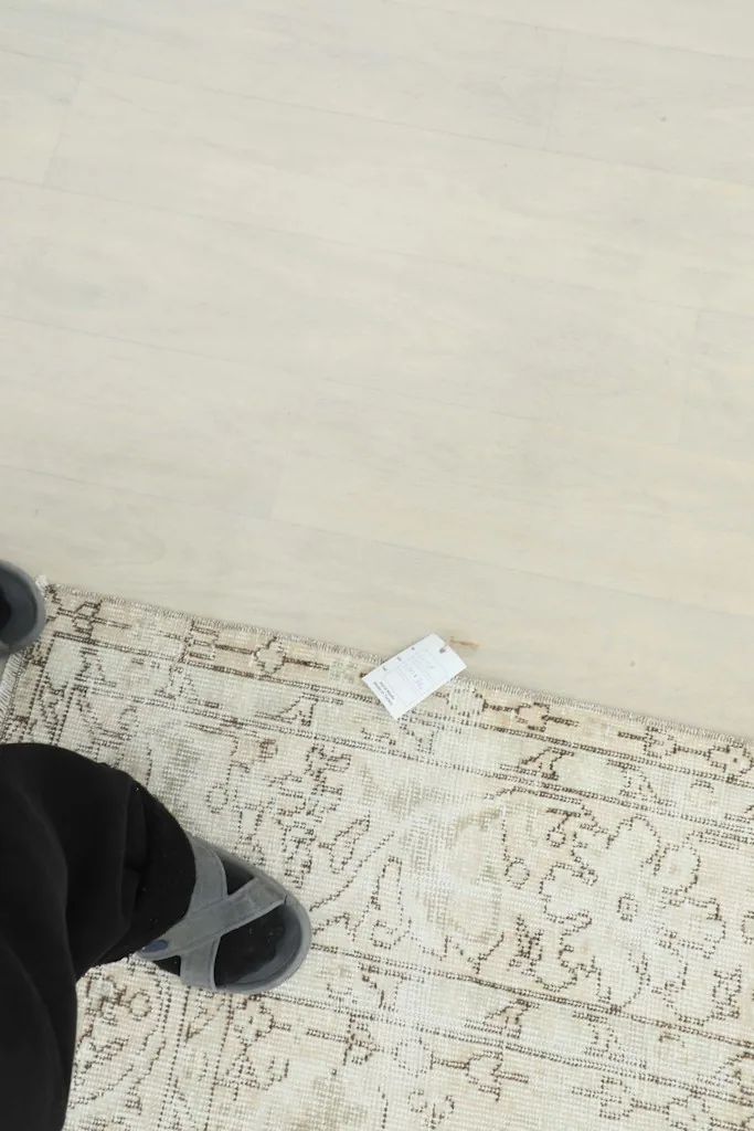 Foot on the rug next to a tag, showing the scale and the soft texture of the vintage wool.