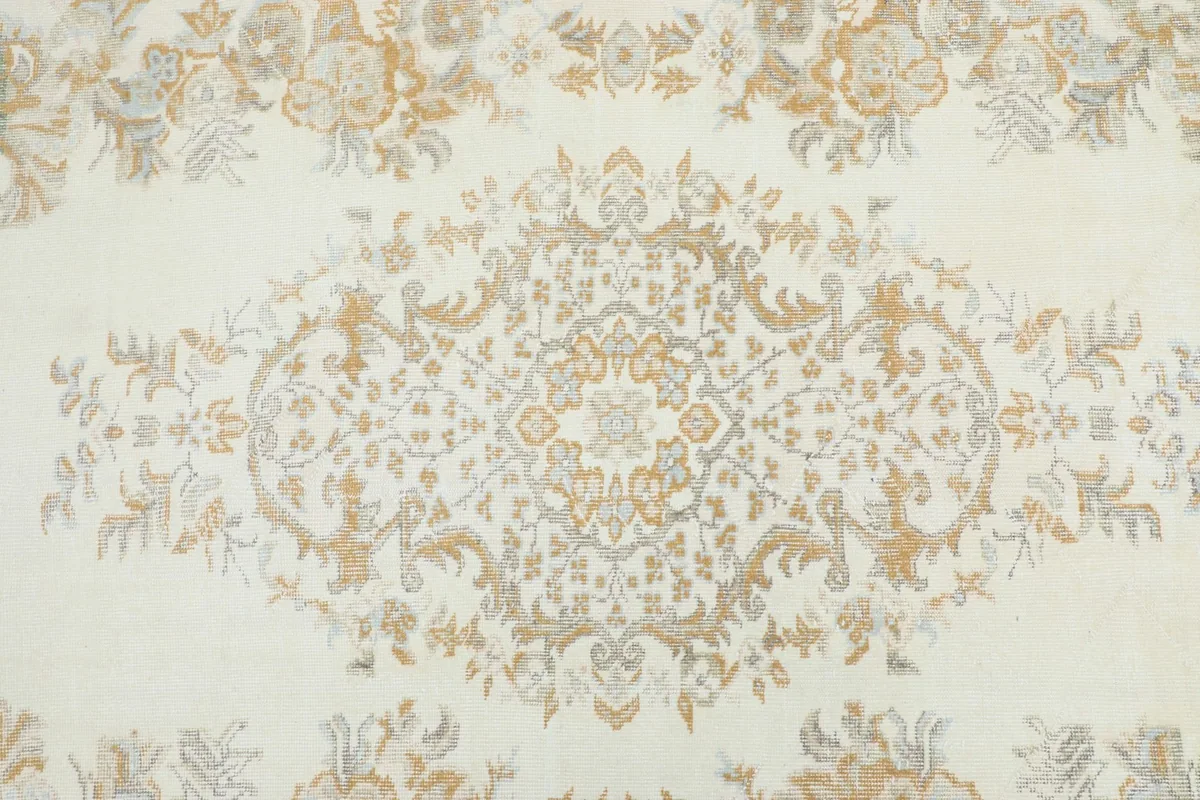 Detailed view of the central medallion and surrounding floral motifs in gold and gray on an ivory field.