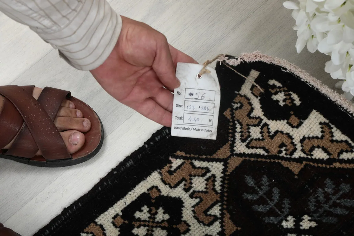 Hand holding a tag showing the rug's details and origin