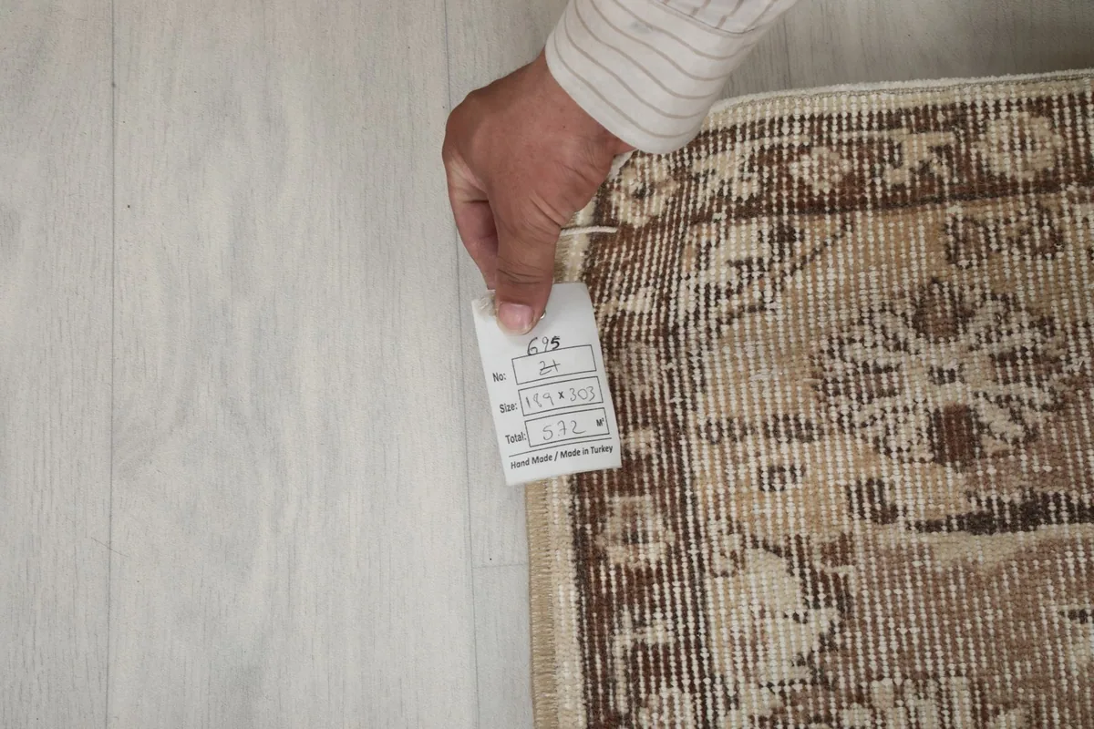 Hand holding a tag with rug details, showing the tightly woven back of the rug