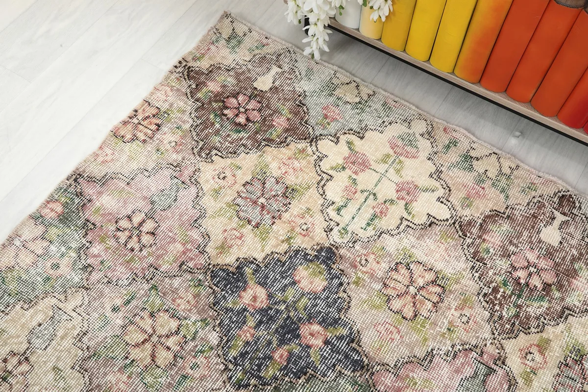 Angle view of the rug from above, showing a blend of muted rose, blue, and beige floral designs