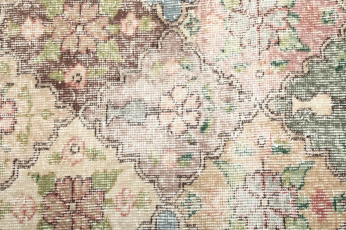 Close-up of the rug's wool pile and distinct floral and geometric motifs in green and brown tones