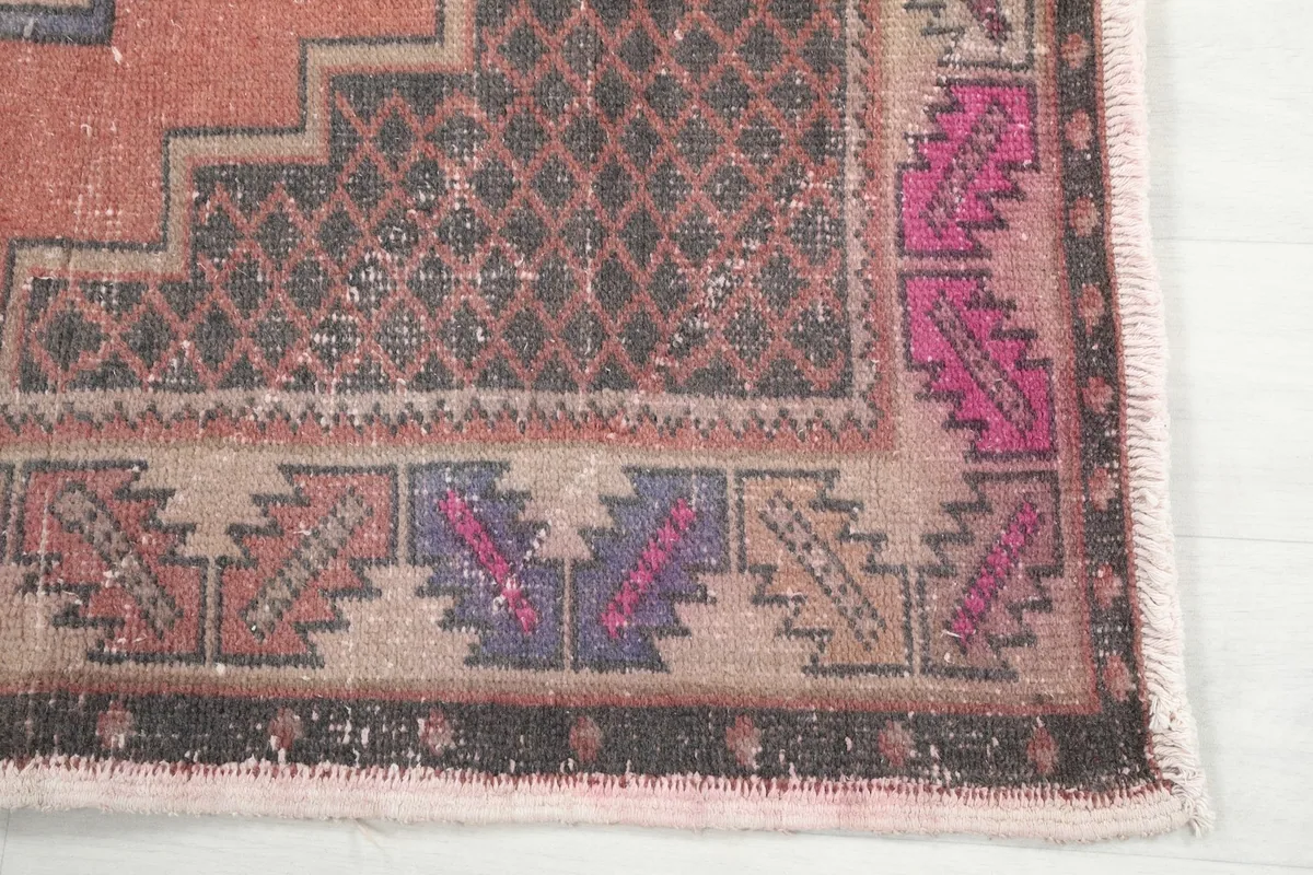 Detailed view of the rug's corner, showcasing the tribal border patterns in brown and pink