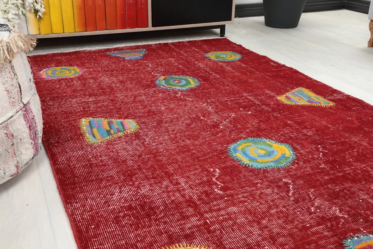 Close-up angled view of the red rug's surface, highlighting the geometric patches and subtle patina
