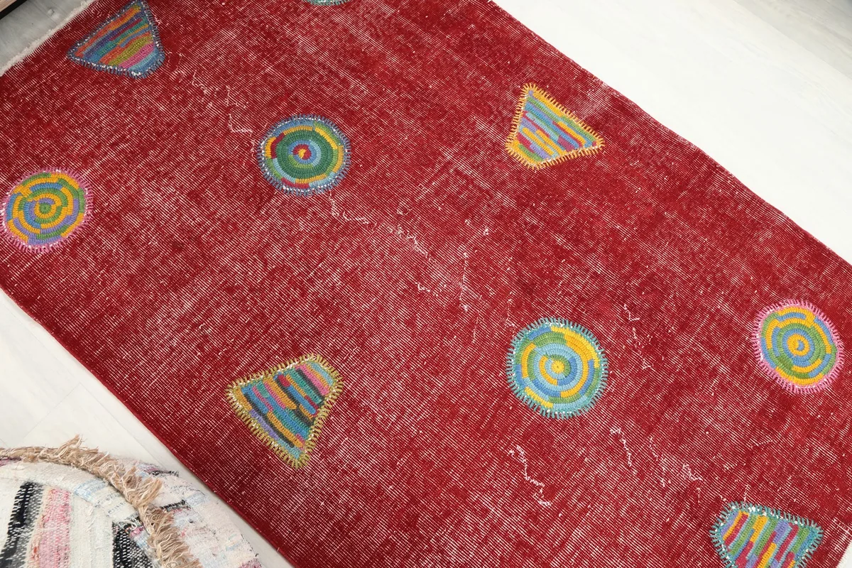 Overhead angled shot of the red vintage rug, showcasing the distribution of its colorful geometric motifs