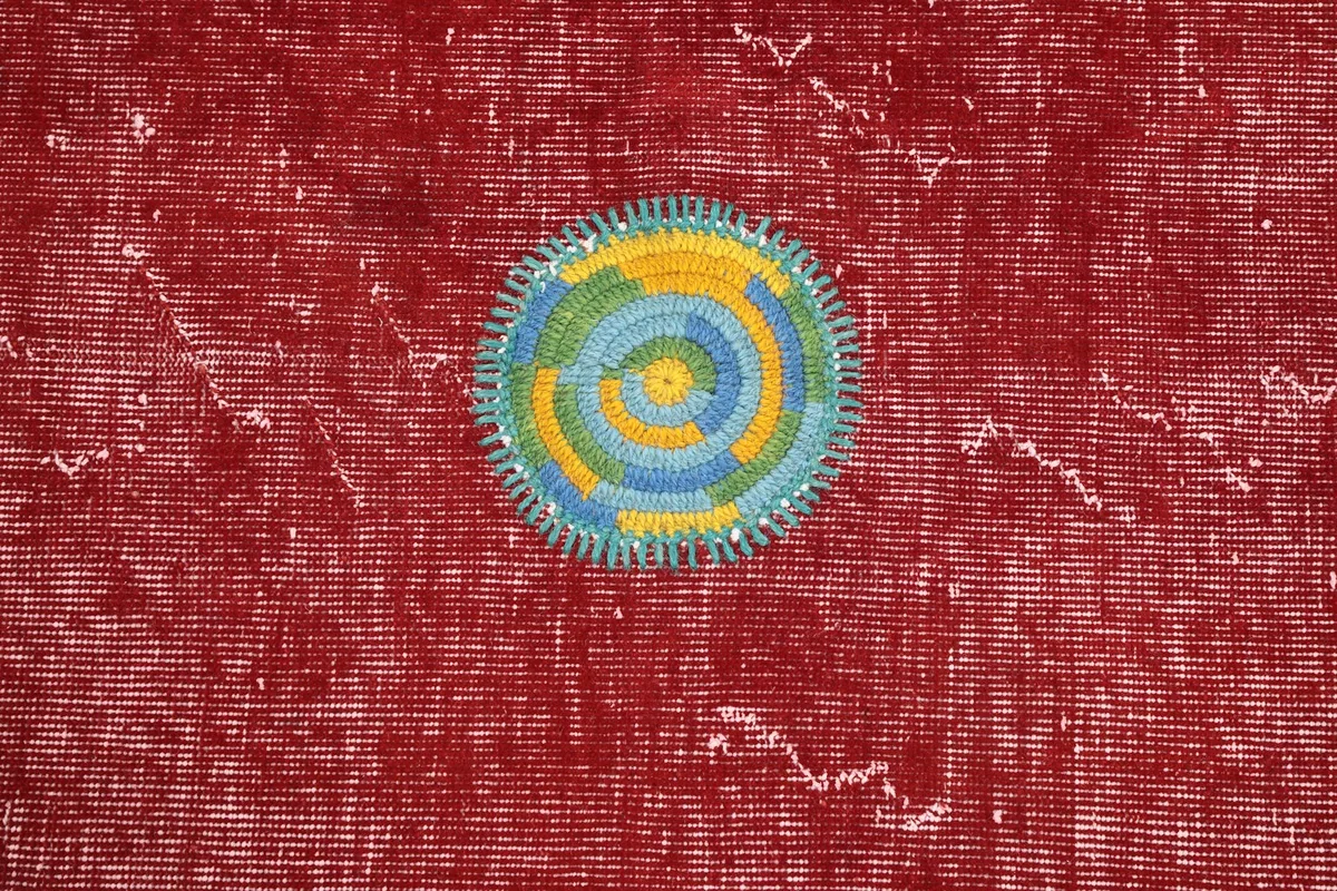 Detailed close-up of a circular patchwork motif in blue, yellow, and green on the red rug