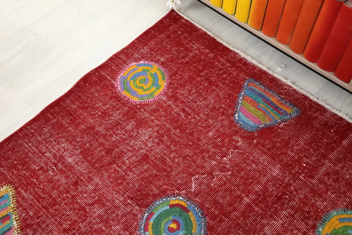 Corner detail of the red rug, showing the worn texture and edge near a colorful bookshelf
