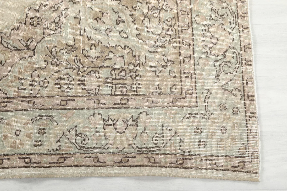 Detail of the rug's outer border with geometric designs and subtle green and brown tones