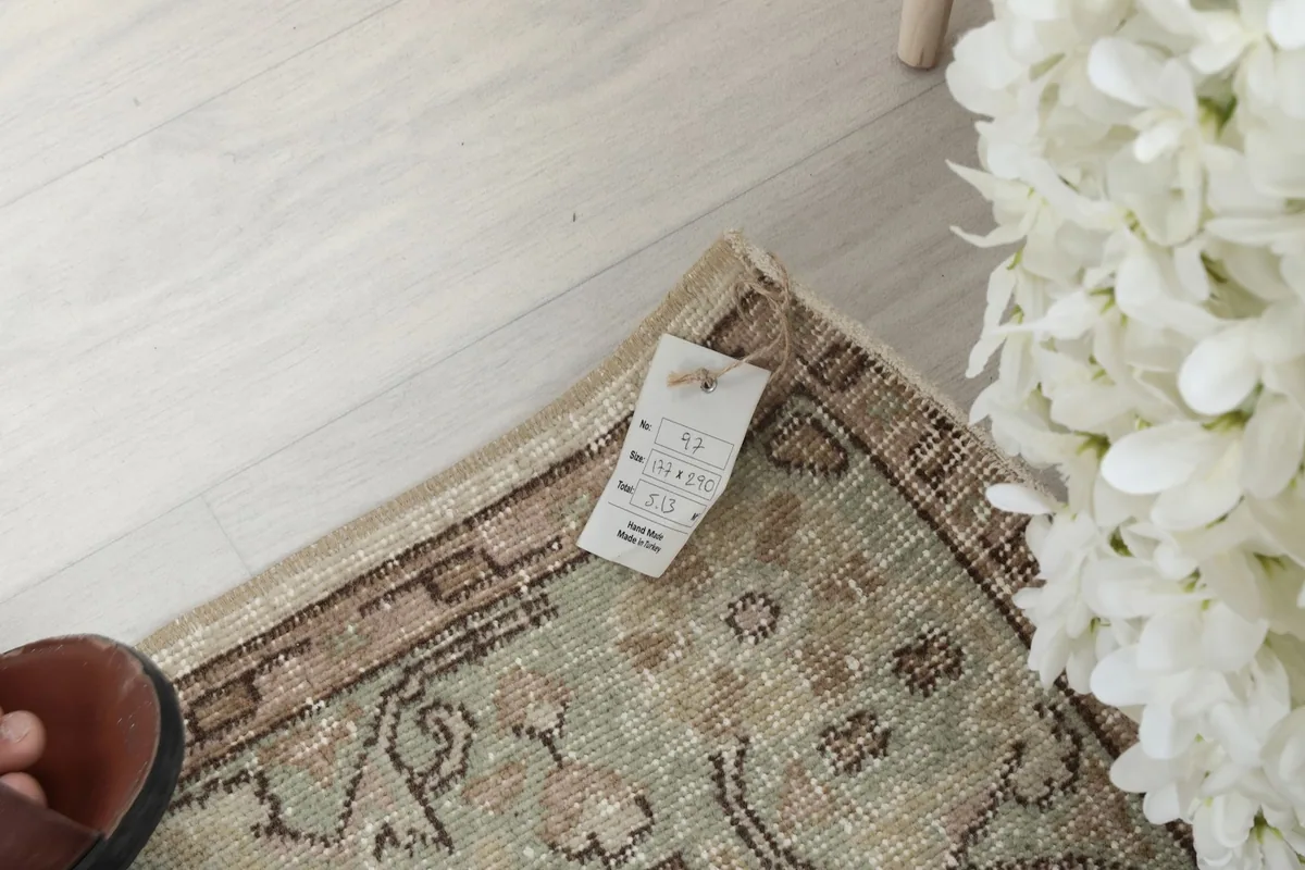 Corner of the rug with a size tag, showing the texture and fringe detail next to white flowers