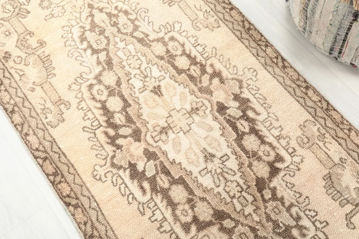 Angled close-up of the rug's central medallion and field colors, emphasizing the beige and brown tones.