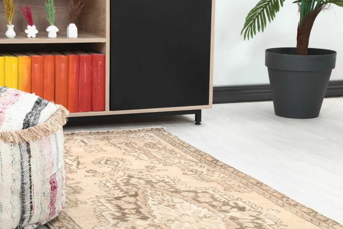 Close-up view of the rug's pattern in a room setting, next to a pouf and bookshelf.