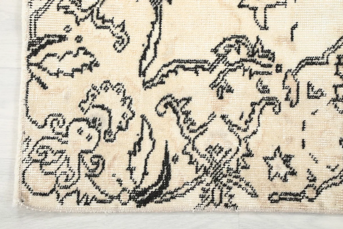 Corner detail of the ivory rug, showing the hand-knotted wool pile and charcoal border design