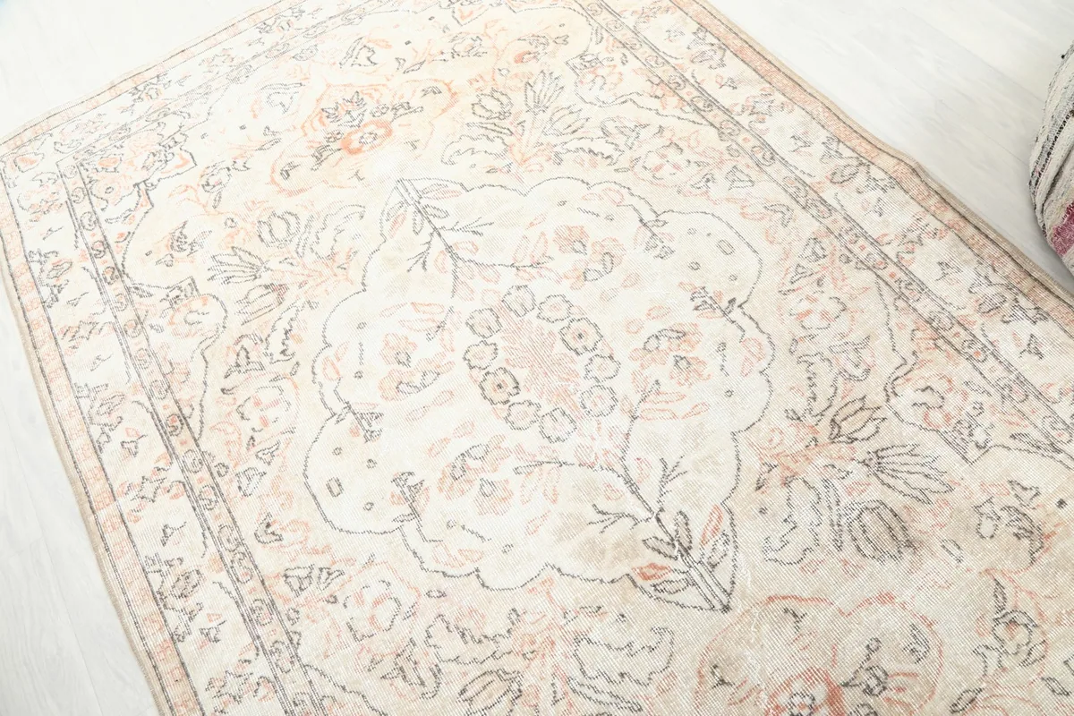 Detailed view of the rug's faded orange and gray floral motifs and ivory background