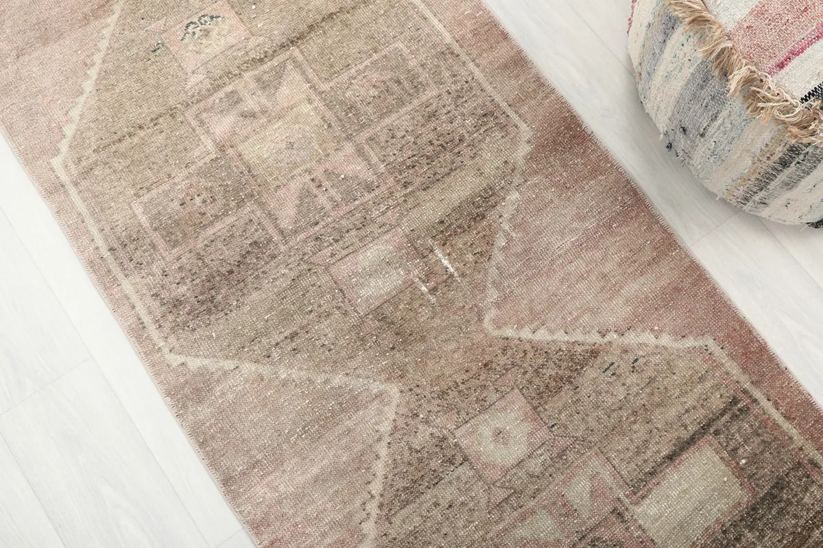 Close-up detail of the rose and brown geometric motifs and natural wear on the runner's pile