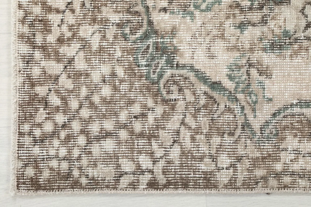 Detail of the rug's outer border, featuring a geometric pattern in brown and gray tones