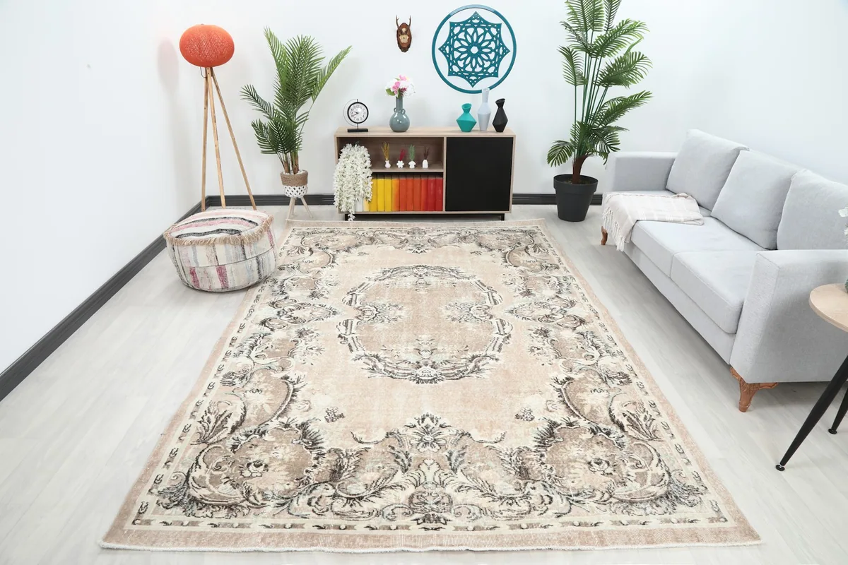 Large vintage area rug in a living room setting with a sofa and plants, showing its full scale.