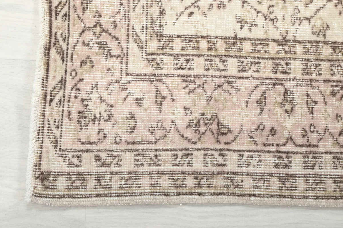 Detail of the rose and beige border with geometric patterns and fringe on the rug