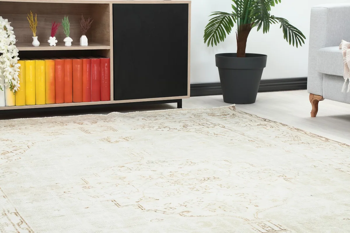 Close-up of the rug's faded ivory and beige patterns near a modern cabinet and plant
