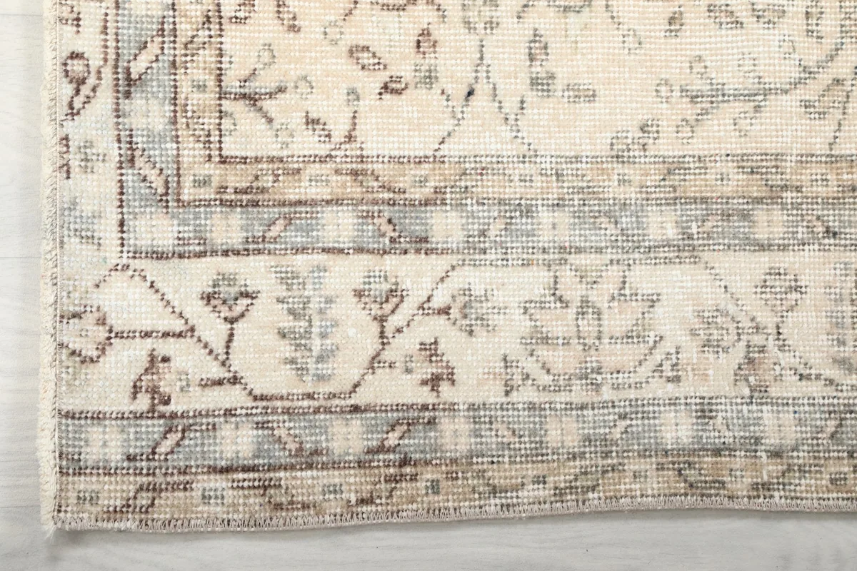Corner detail of the ivory rug, showing the intricate border design with muted beige and gray tones.