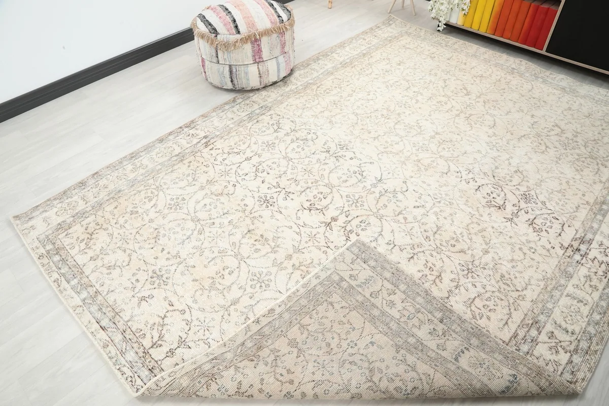Corner of the ivory vintage rug slightly folded back, revealing the reverse side and construction.