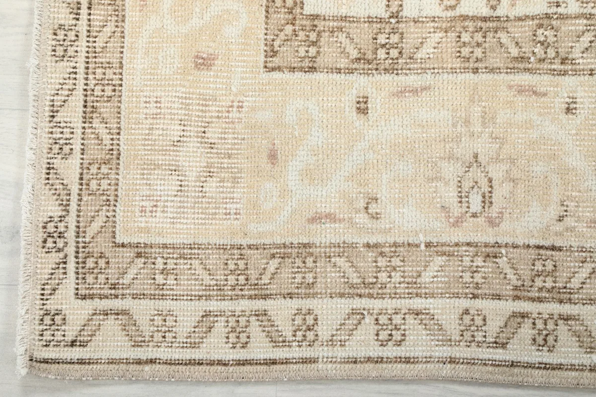 Detail of the rug's border, showing the geometric and floral motifs in beige and brown tones