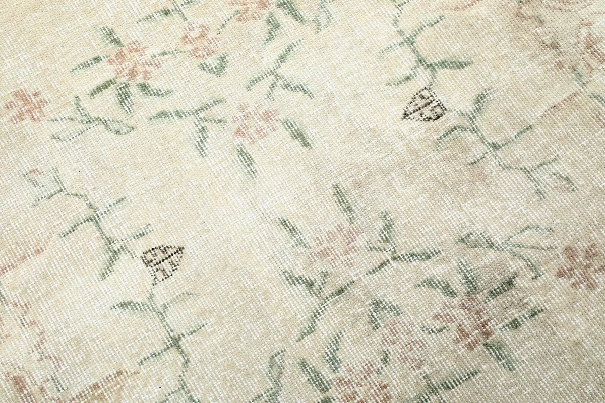 Close-up of the delicate floral and vine motifs in rose and green tones on the rug's surface.