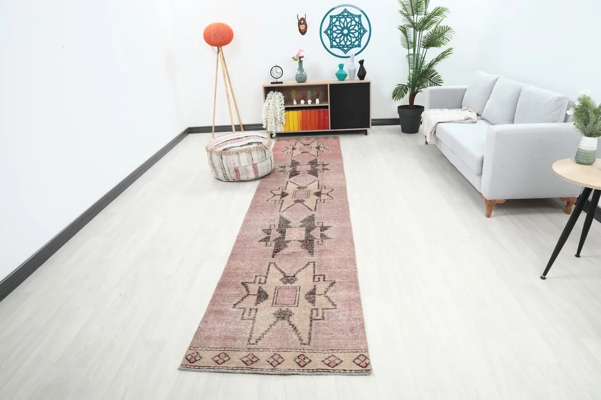 Vintage runner rug displayed in a room setting, showing its length and rose and beige colors.