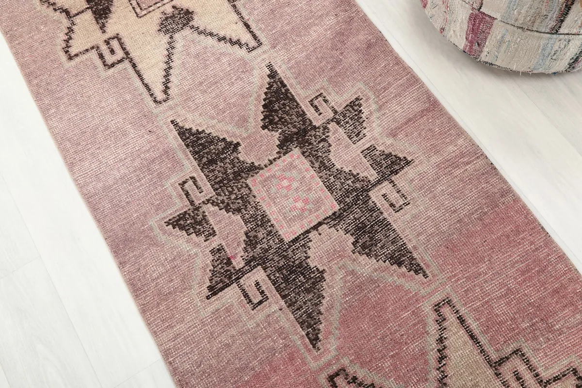 Detailed angled shot of the rose and charcoal geometric patterns on the vintage runner rug.