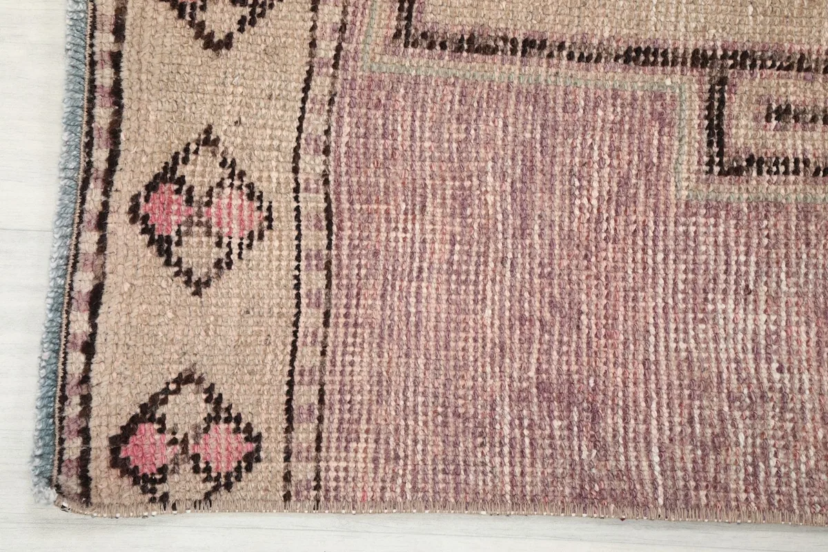 Detail of the rug's border design featuring small diamond motifs in beige, rose, and charcoal.