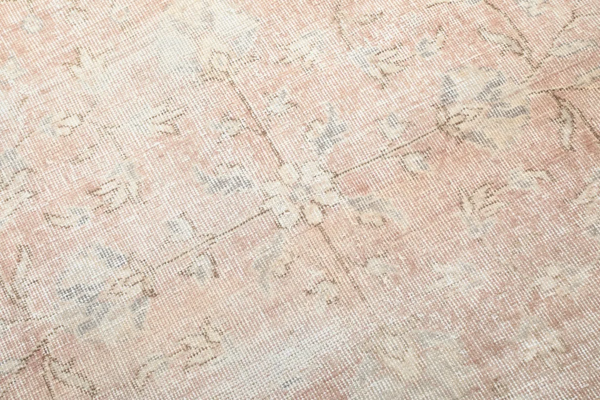 Close-up detail of the hand-knotted wool pile, showing faded rose and beige tones with motifs