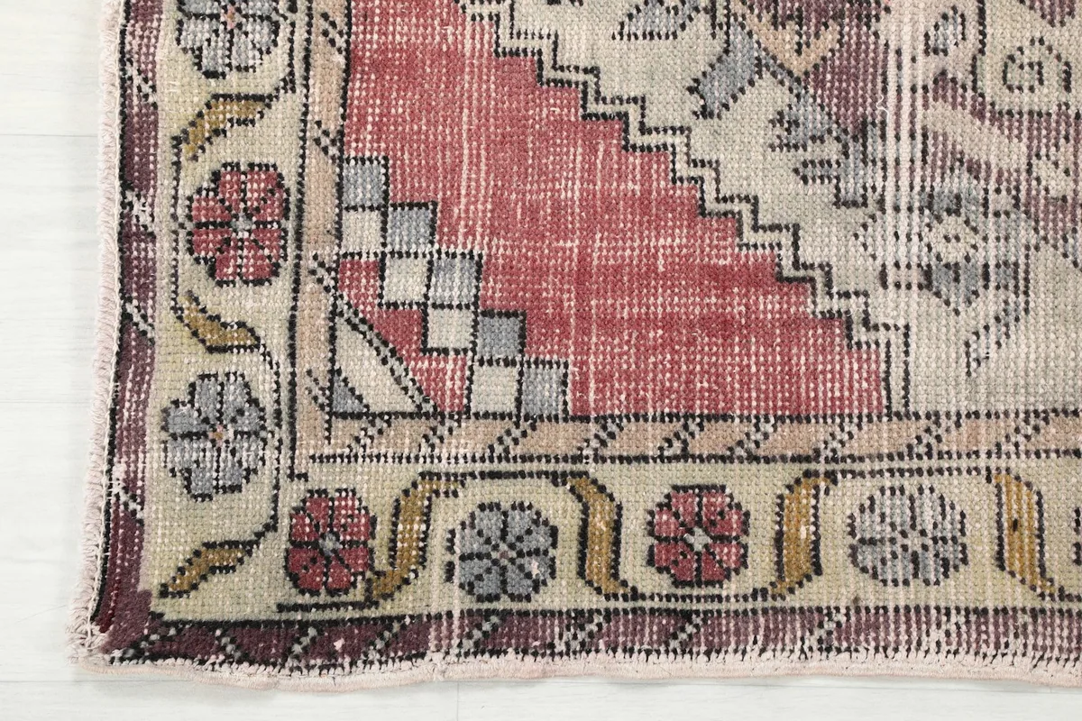 Close-up of the rug's end border, showing the floral and geometric elements in rose, beige, and gray.