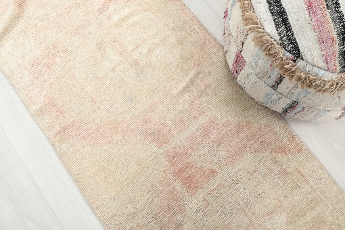 Close-up detail of the hand-knotted wool pile, showing the faded cream and rose geometric motifs