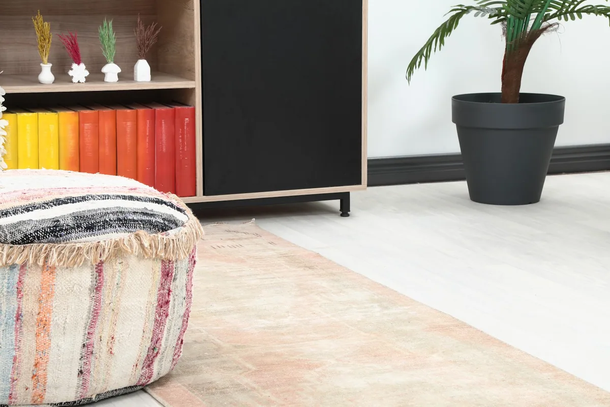 Close-up of one end of the rose and gray runner rug on the floor next to a colorful pouf and shelving.