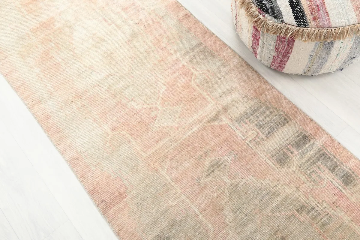 Close-up showing the subtle rose, gray, and beige tones and the worn texture of the vintage runner rug.