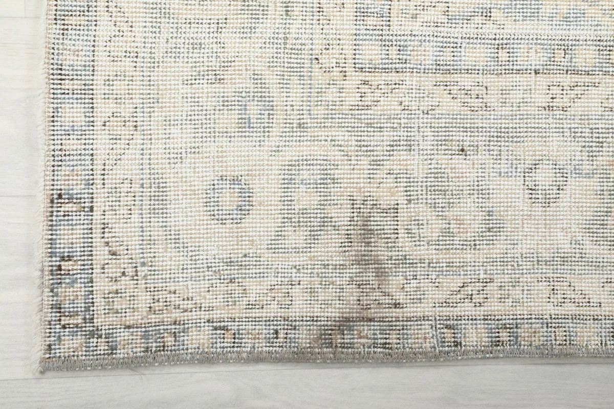 Close-up of the rug's border pattern showing the muted blue and beige threads.