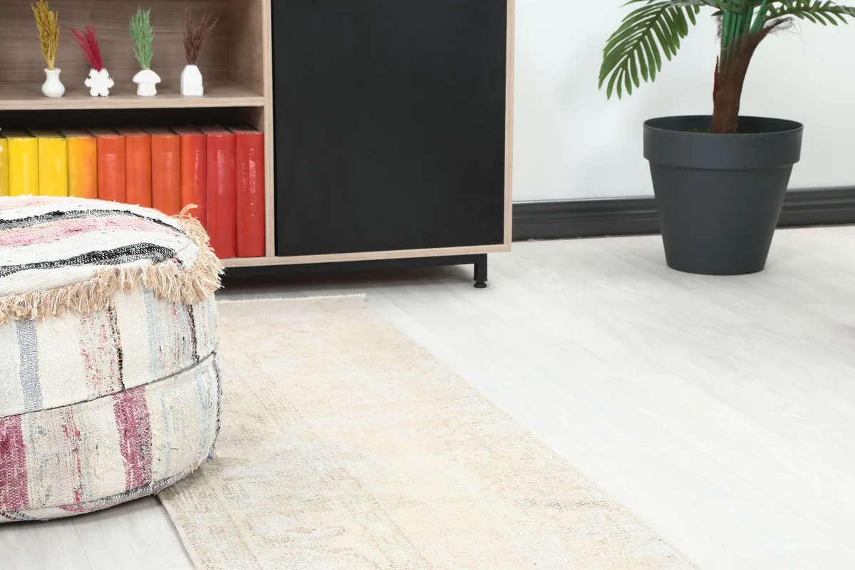 Close-up of the cream runner rug on the floor next to a colorful pouf and a wooden cabinet