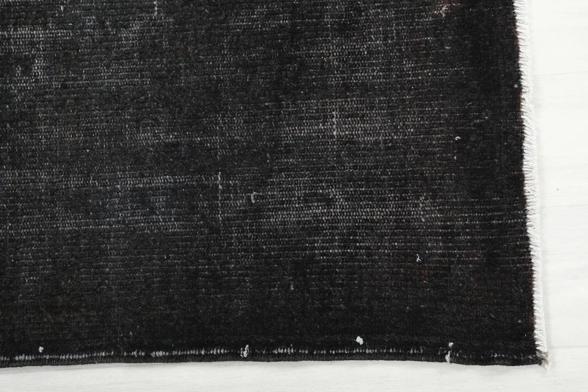 Detailed view of a corner of the charcoal rug, revealing the woven edge and the blend of black and gray fibers.