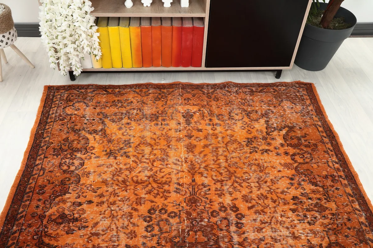 Overhead shot of the orange rug in a room setting, positioned in front of a cabinet.